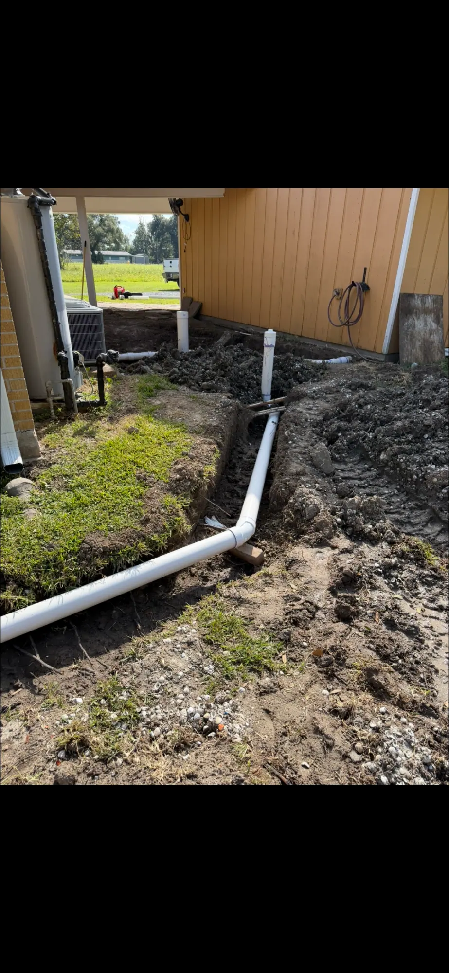 White pipe run in a trench beside a house wall